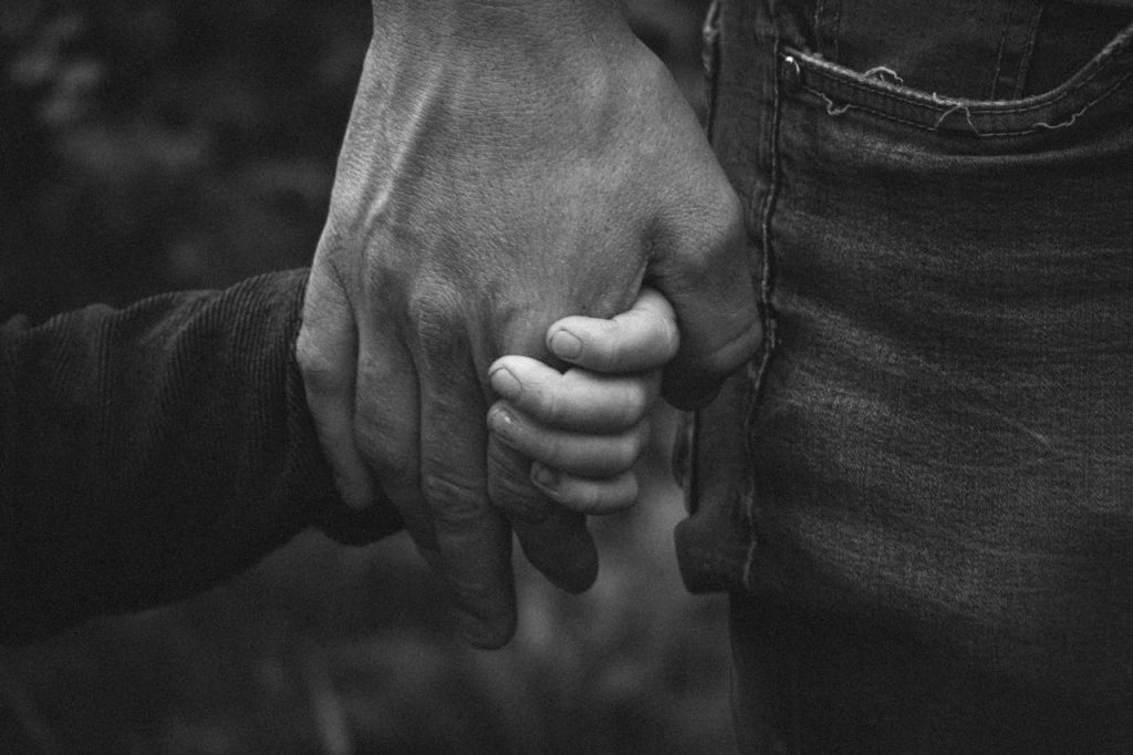 A touching black and white photo of a father holding his child's hand, symbolizing love and connection.